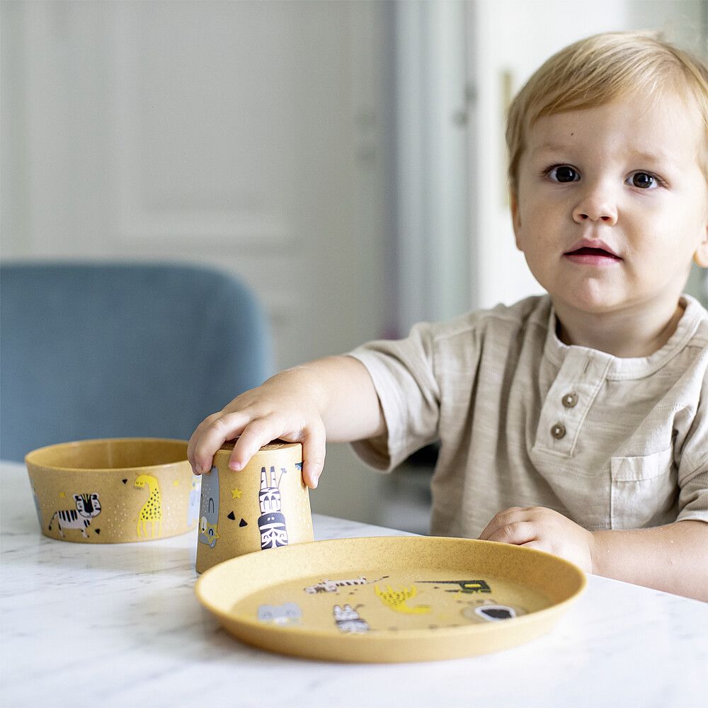 Klein Kind was an einem Tisch sitzt mit Kinder Teller, Schüssel und Becher vor sich