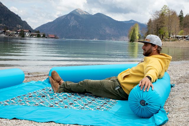 Mann auf Decke mit Rückenpolster am Seeufer