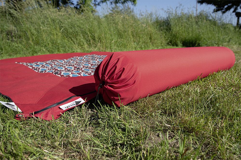 9961696700 BENT Kissenrolle, rot mit Teppich auf einer Wiese
